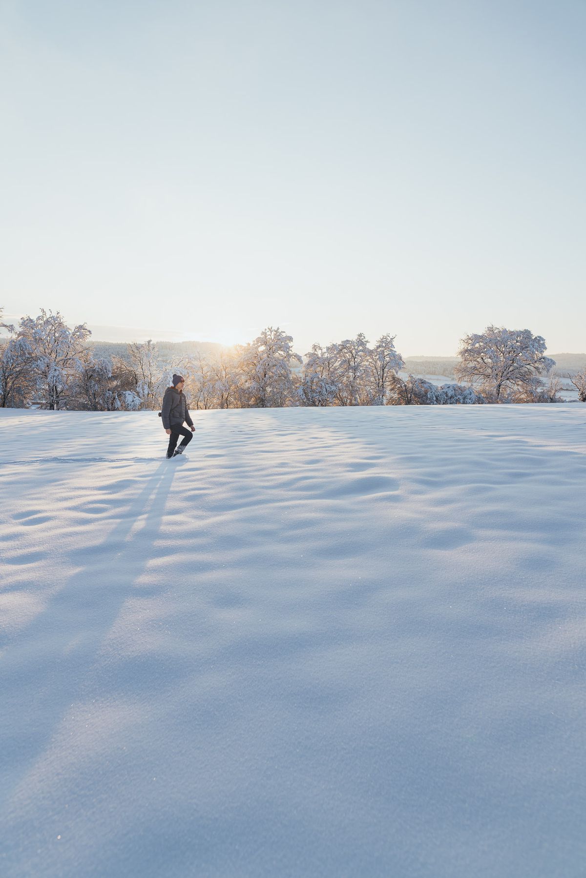 Lone figure crossing a snowfield at sunrise